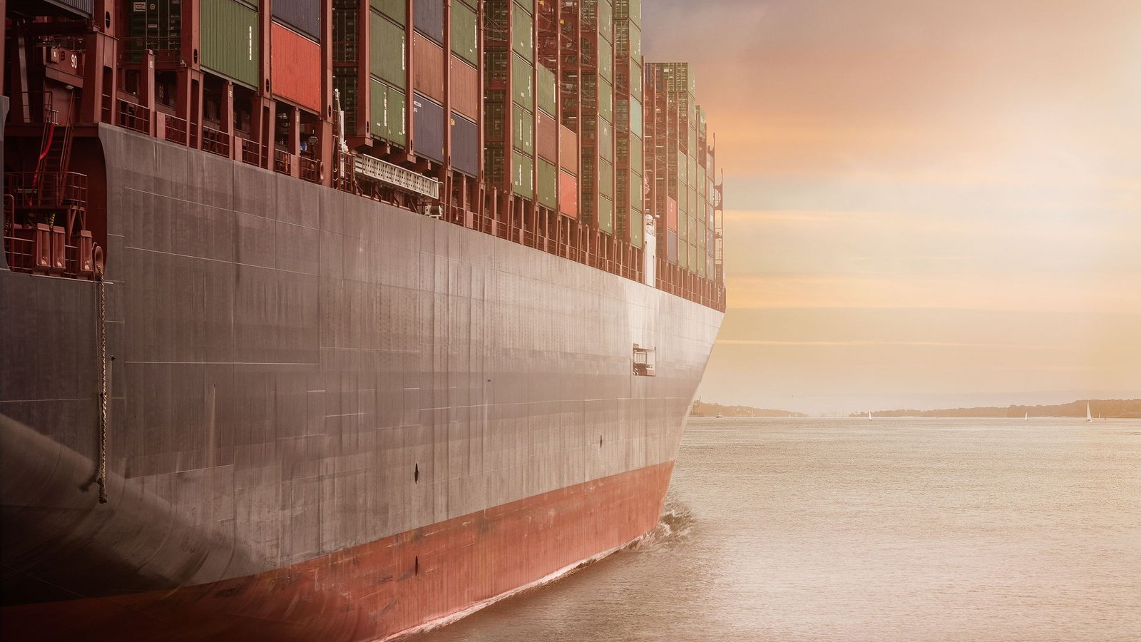 Container ship berthed at a port terminal beneath gantry cranes at sunset