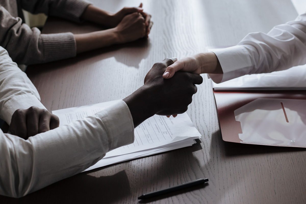 Two business partners shaking hands over contract documents on a desk