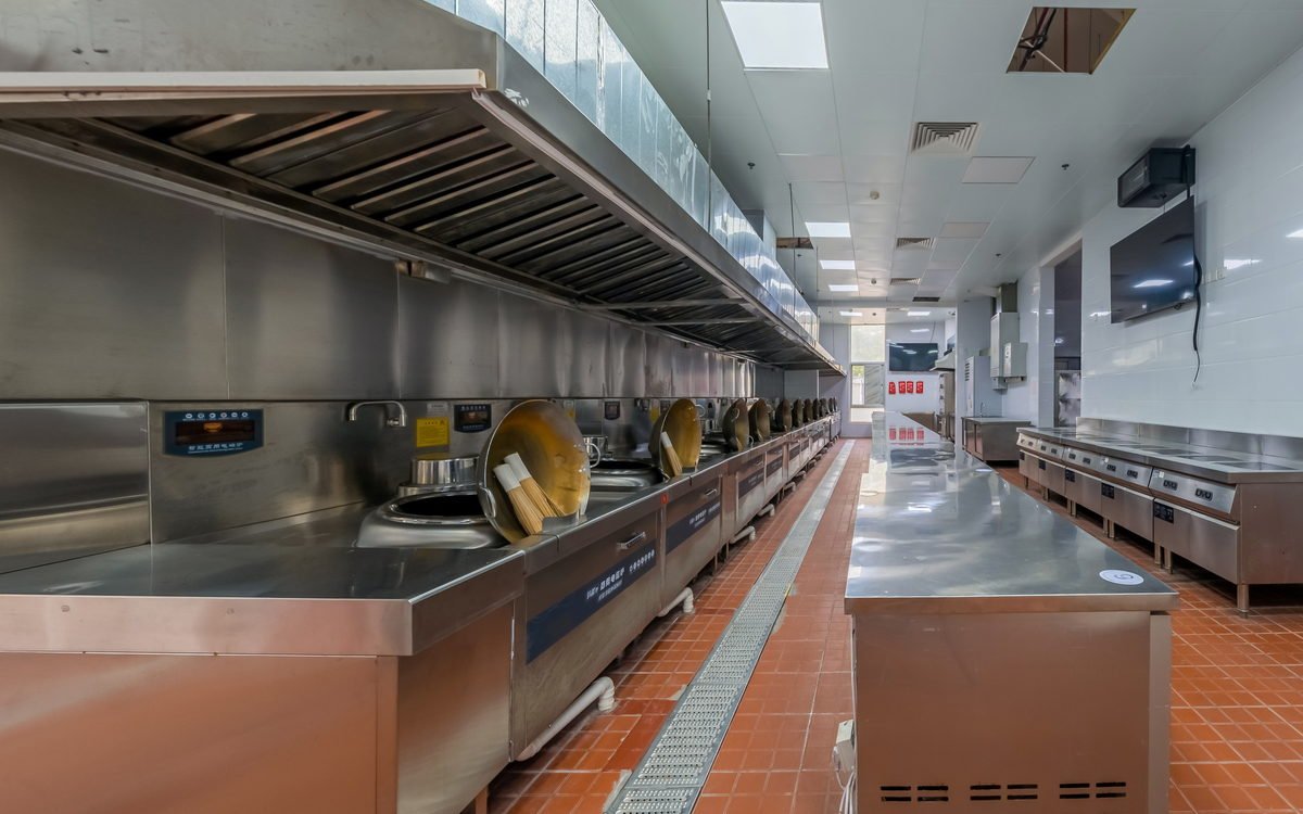 Stainless steel commercial kitchen line with extraction hoods and cooking stations